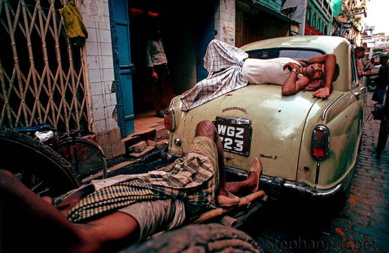 2 men are sleeping in street. One of them are sleeping on top of his car. Kolkata-India